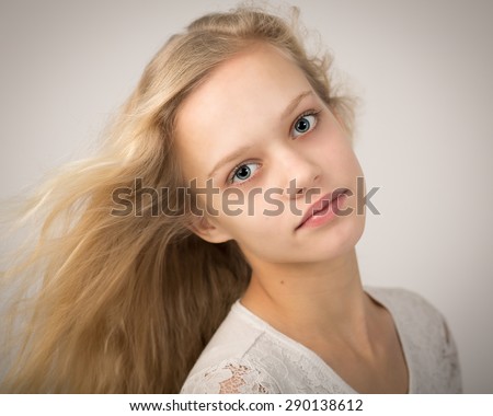 Portrait in the studio of a beautiful blond girl with blue eyes and long hair blowing in the wind isolated against a grey background.