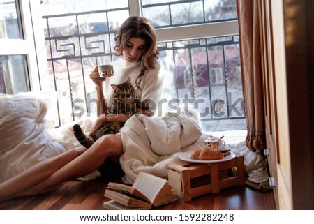 Beautiful woman playing with cat at comfort makeshift bed at the morning near the open balkony window and take a breakfast at the background roofs of houses in the sun. Zdjęcia stock © 
