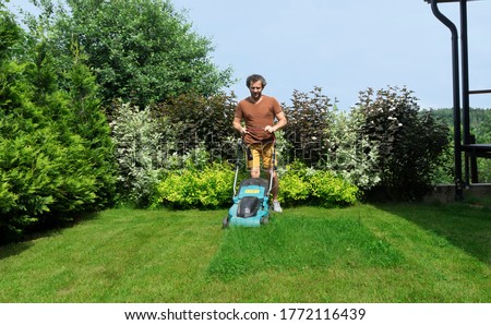 Lawn mowing in a beautiful landscape. An adult man using a lawn mower with a grass catcher mows overgrown grass on the lawn. Foto stock © 