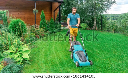 Lawn care. Mowing grass with an electric lawn mower. A young man mows the grass with a lawn mower with a grass collector on a sunny summer day. Beautiful landscape design in the garden.