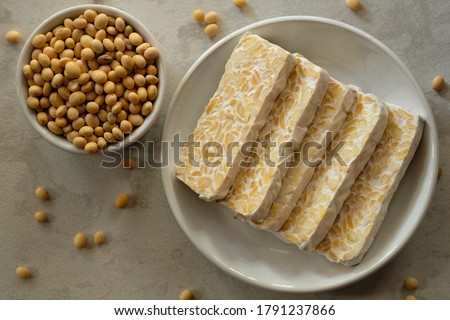 Raw tempeh or tempe. tempeh slices in white ceramic bowls and on a marble table. raw soybean seeds in a white ceramic bowl. Tempe is a traditional Indonesian food made from fermented soybeans.