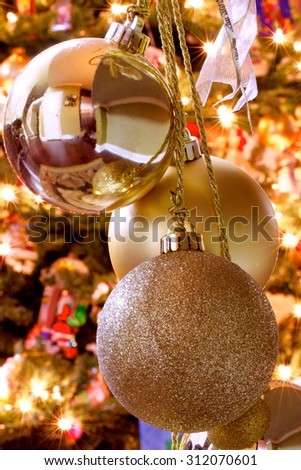 Gold Christmas bauble ornaments on gold strings in front of the warm lit glow of a Christmas tree.