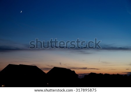 Navy dusk with crescent moon over silhouettes of neighboring houses with rolling clouds.