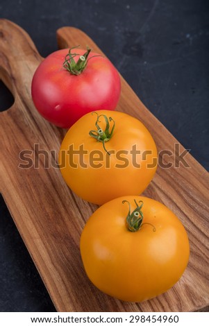 Fresh tomatoes on cutting board on black table, studio shot
