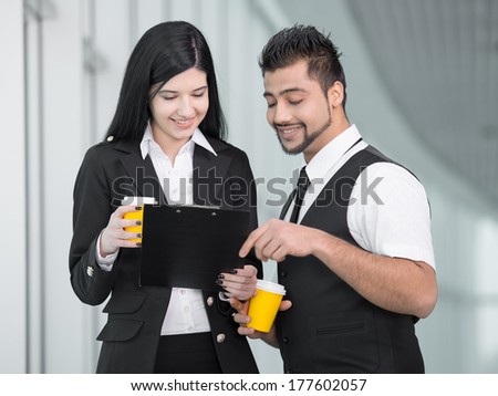 Confident businesswoman and businessman standing in office and drink coffee