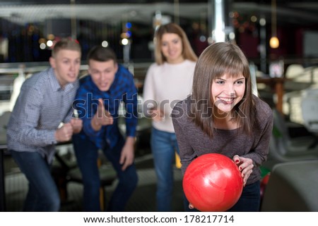 Group of four friends in a bowling alley having fun, three of them cheering the one girl in charge to throw the bowling ball
