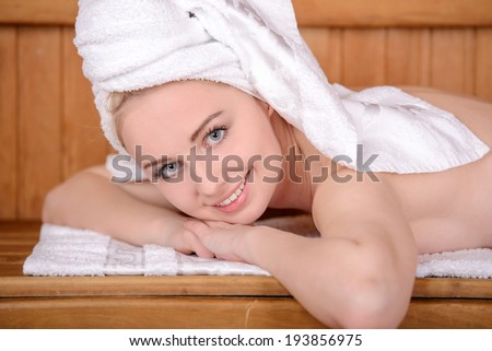 Beautiful woman in sauna. Attractive young woman wrapped in towel relaxing in sauna and smiling to you