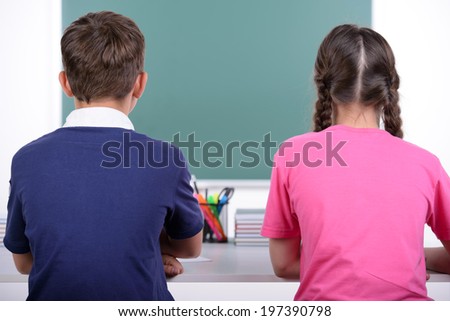 Studying together. Rear view of two little classmates reading a book together