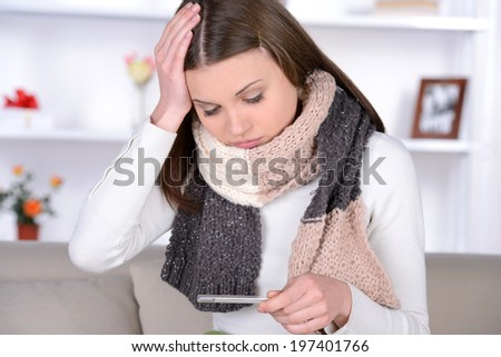 Checking body temperature. Young woman covered with plaid checking her body temperature while sitting in bed at her apartment
