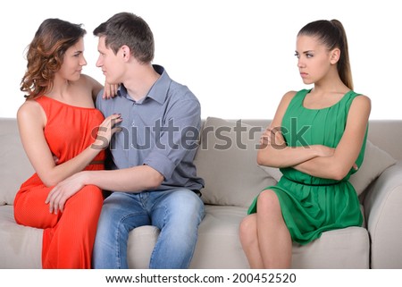 Jealousy. Young sad women sitting on the couch with her arms crossed while another women and men hugging near her