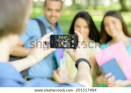 Group of happy young college students do photography at mobile phone in the park