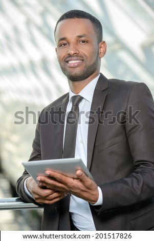 Join the digital age. Cheerful young African working with tablet in office center