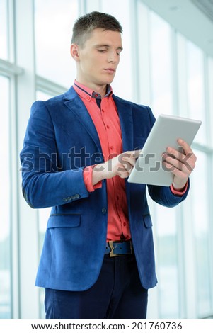 Portrait of a young businessman holding a tablet stood in the hallway at the office