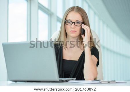 Business woman at work. Confident young business woman talking on the phone and using computer while sitting at her working place