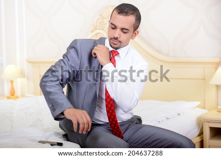 Portrait of Asian businessman with a suitcase sitting on the bed and wear a jacket in the hotel room