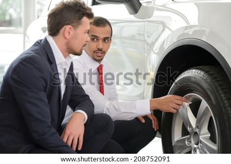 Look at these tires! Young car salesman showing the advantages of the car to the customer