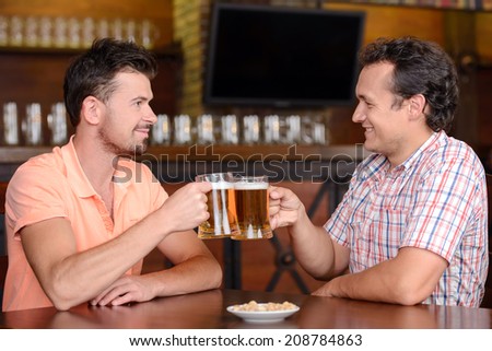 Friends in beer pub. Two cheerful friends drinking beer and talking at bar