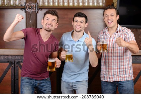 Friends cheering. Three happy soccer fans drinking beer at the pub