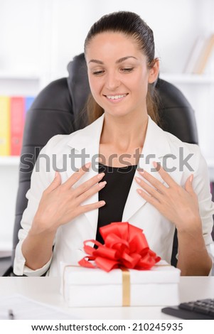 Happy and smiling young business woman at the desk with a laptop opens a box with a gift
