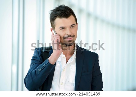 Business man talking on phone traveling walking inside in airport. Casual young businessman wearing suit jacket and shoulder bag.
