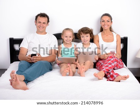 Modern technology in home. Young family, the use of tablets and phones, lying in bed at home