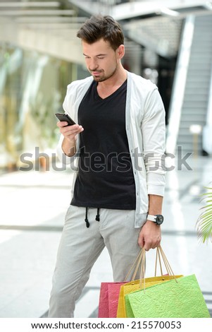 Shopping. Young handsome man with bags for shopping talking on the phone in a shopping center