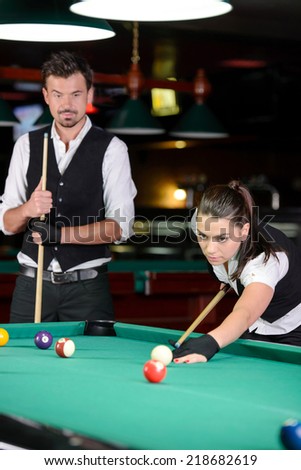 Young man and woman playing professional billiards in the dark billiard club