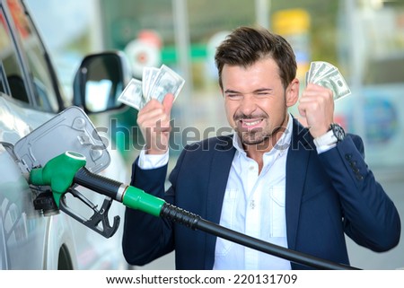 Emotional businessman counting money with gasoline refueling car at fuel station