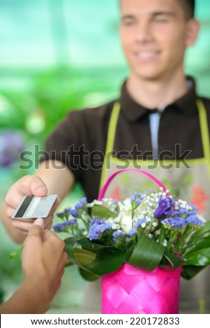 Young man working as florist giving credit card to customer after purchase.