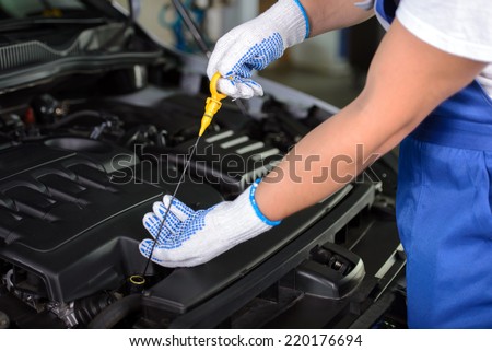 Side view of mechanic checking motor oil in a car with open hood