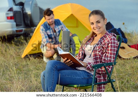 Attractive happy woman sitting near tent cities holding book on a sunny day