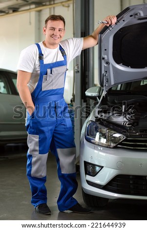 Mechanic in auto repair shop standing next to car with open hood