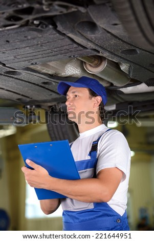 Car mechanic examining car suspension of lifted automobile at repair service station