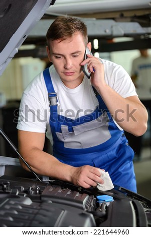 Auto mechanic using mobile phone in workshop, at car