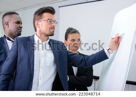 Young multiethnic business team planning a new strategy standing grouped in front of a flip chart analyzing a chart