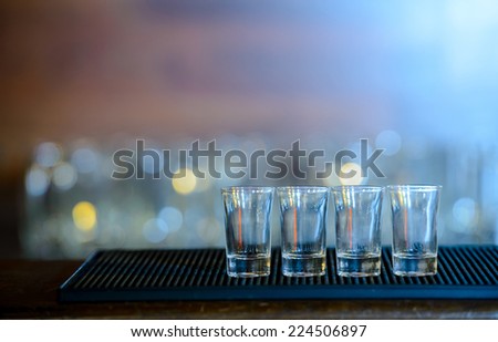 Four shots of tequila on a wooden table bar on the background of bright lights of the bar