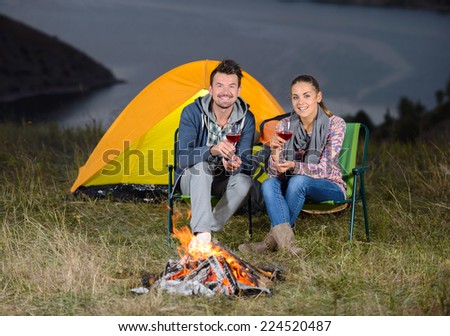 Romantic evening. Charming couple near a fire while camping drinking wine