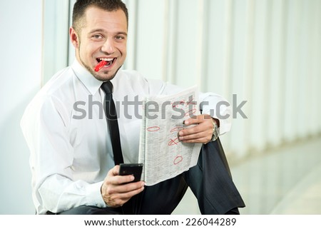 The concept of job search. A smiling man is sitting with a newspaper and pen.