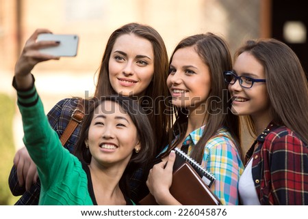 Portrait of female students that are making pictures with university building in the background.