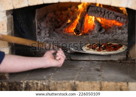 Close-up. Chef inserts the pizza inside the wood oven to bake.