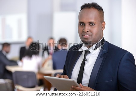 Portrait of black businessman, people group in background at modern bright office indoors