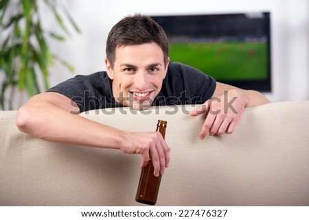 Smiling young man with a beer while watching the game sitting on sofa.