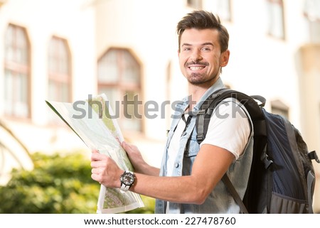 Trendy young man in the town with touristic map and backpack.