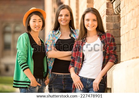 Portrait of young smiling female students with university building in the background.