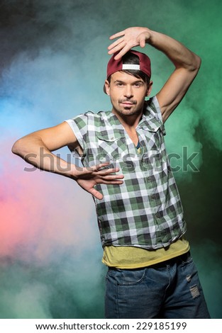 Young stylish man, hip hop dancer on the colored foggy background.