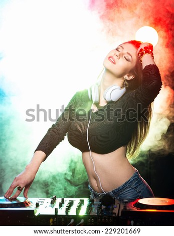 Portrait of a young female DJ at work, the club lights on the background.