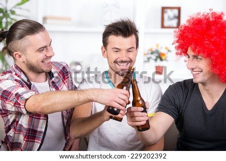 Group of happy sports fans are watching game on TV at home and drinking beer.