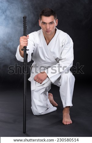 A martial arts man with a sword sat down on one knee.