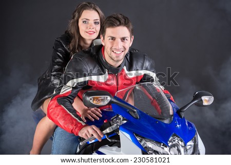 Motorcyclist in black and red equipment and young smiling woman on dark background.