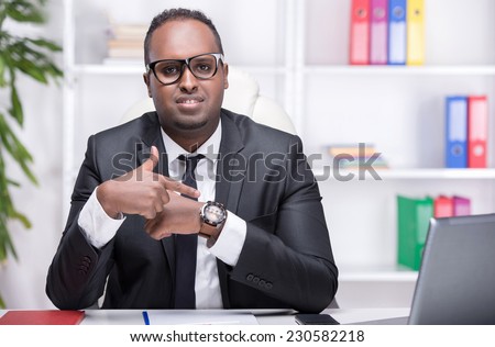 Portrait of young businessman at work, is pointing at the clock on his arm.